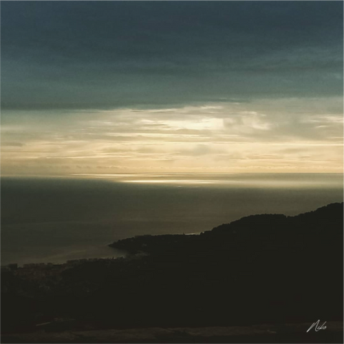 Photographie d'art en clair-obscur : mer et reliefs se fondant dans l'ombre, clarté diffuse à l'horizon
