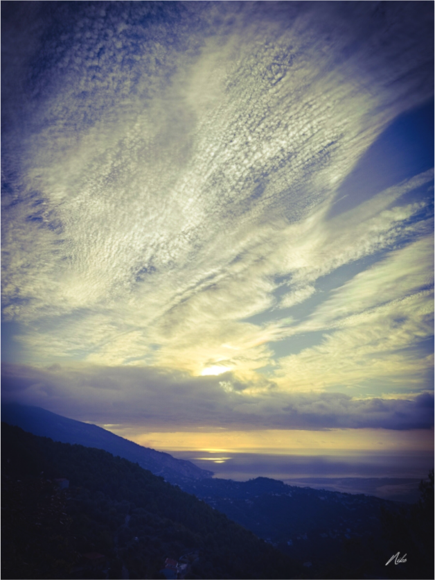 Photographie d'art verticale : ciel traversé de lumière au-dessus de la mer, terre sombre à l'horizon