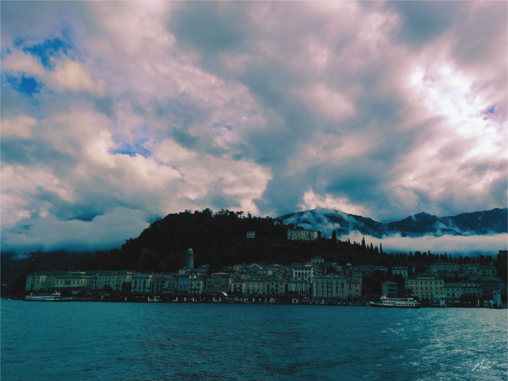 Photographie d'art de lac de montagne : rive s'effaçant entre nuages, montagne et eau sous un ciel immense