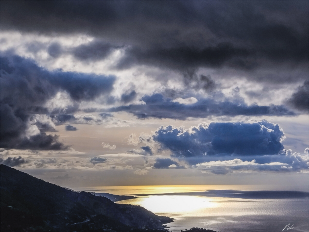 Photographie d'art en clair-obscur : trouée de lumière sur la mer sous un ciel chargé, reliefs dans l'ombre